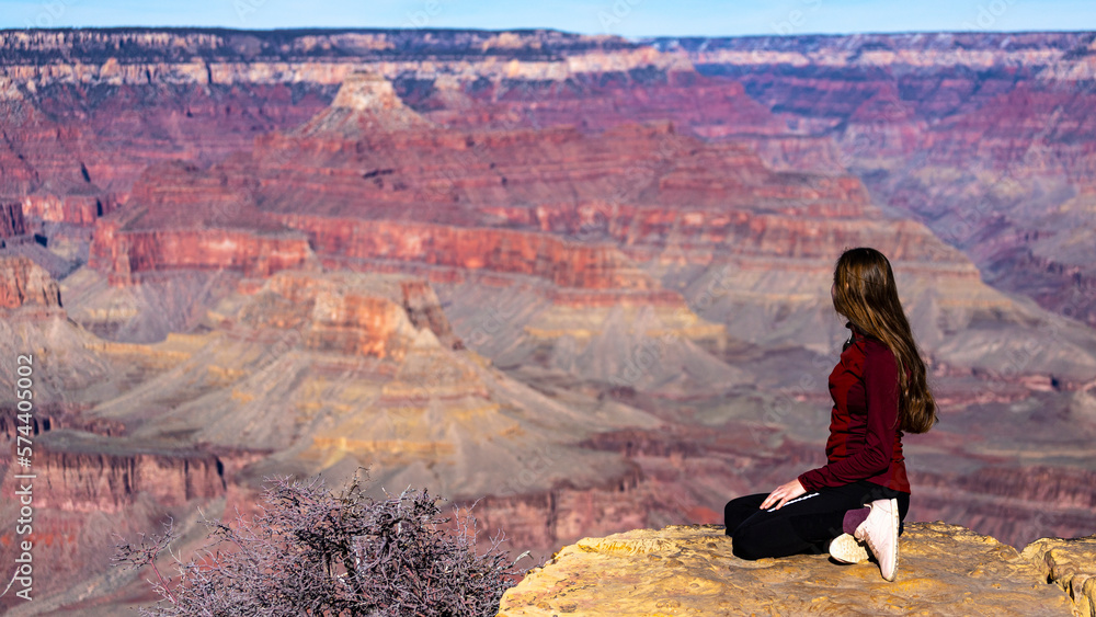 Rear view of a long-haired girl sitting on the edge of the grand canyon admiring the unique landscape; panorama of the grand canyon national park 
