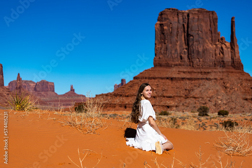 portrait of a girl in a lace dress sitting on the sand in monument valley with massive rocks in the background; cowgirl in the American desert in the wild west