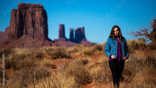 girl in denim jacket walks through monument valley with massive monuments in the background; walk in the wild west, scene from a western