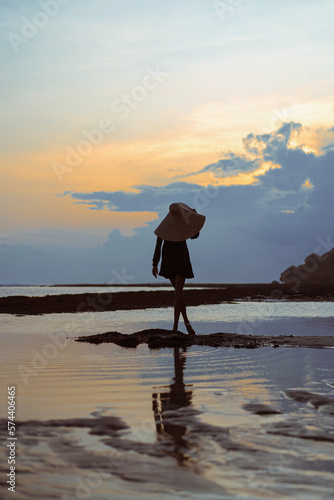 Young woman in a big straw hat on the ocean at sunset.
