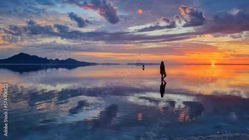 Silhouette of woman walking into the sunset of lake Bonneville Salt Flats, Wendover, Western Utah, USA, America. Beautiful summits of Silver Island Mountain range reflecting in water surface. Awe © Chris