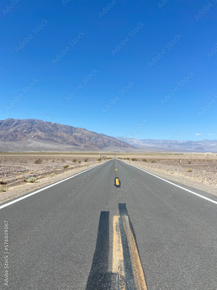 State Route 190 near the Devil's Cornfield area in Death Valley National Park, California, United States. Empty desert road in Death Valley with clear blue sky and rocky mountains. State Route 190 near the Devil's Cornfield area in Death Valley National Park, California, United States. Empty desert road in Death Valley with clear blue sky and rocky mountains.