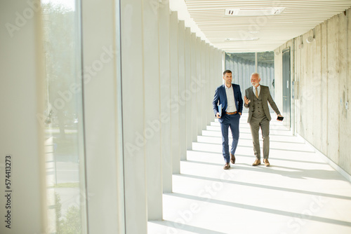 Young and a senior businessman walk down an office hallway, deep in conversation © BGStock72
