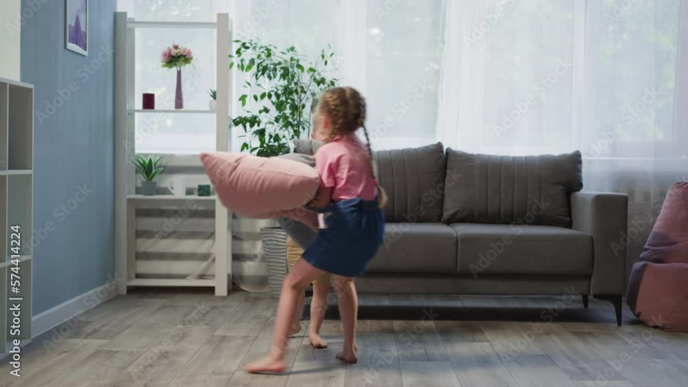 Active siblings jump fighting with pillows in cozy living room. Disobedient toddler and preschooler girl disturb order in house on weekend Active siblings jump fighting with pillows in cozy living room. Disobedient toddler and preschooler girl disturb order in house on weekend