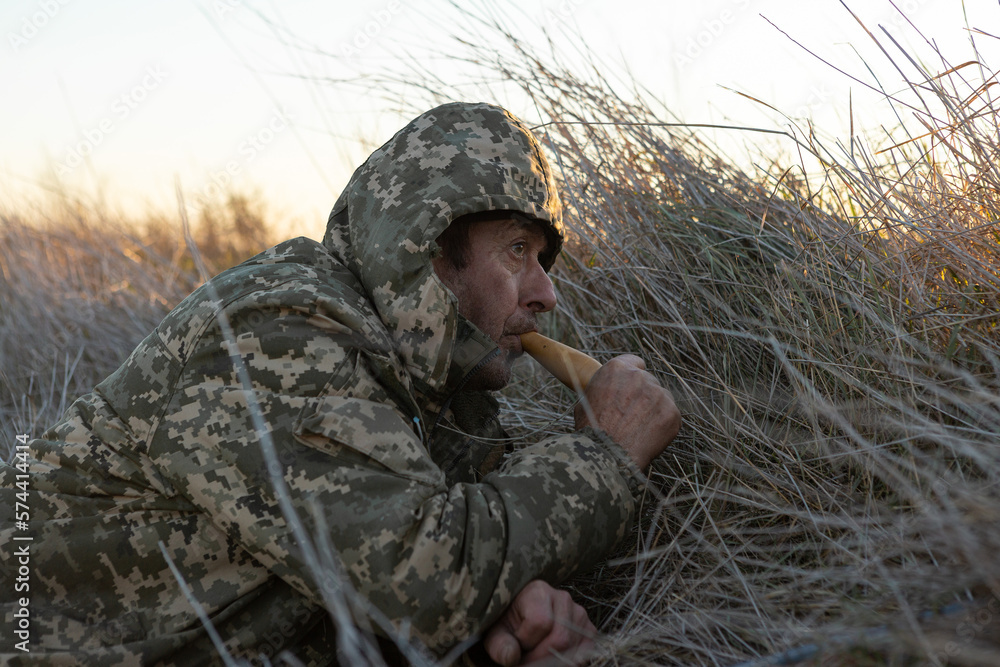 A mature hunter with a gun lures ducks by decoy while sitting in the reeds A mature hunter with a gun lures ducks by decoy while sitting in the reeds