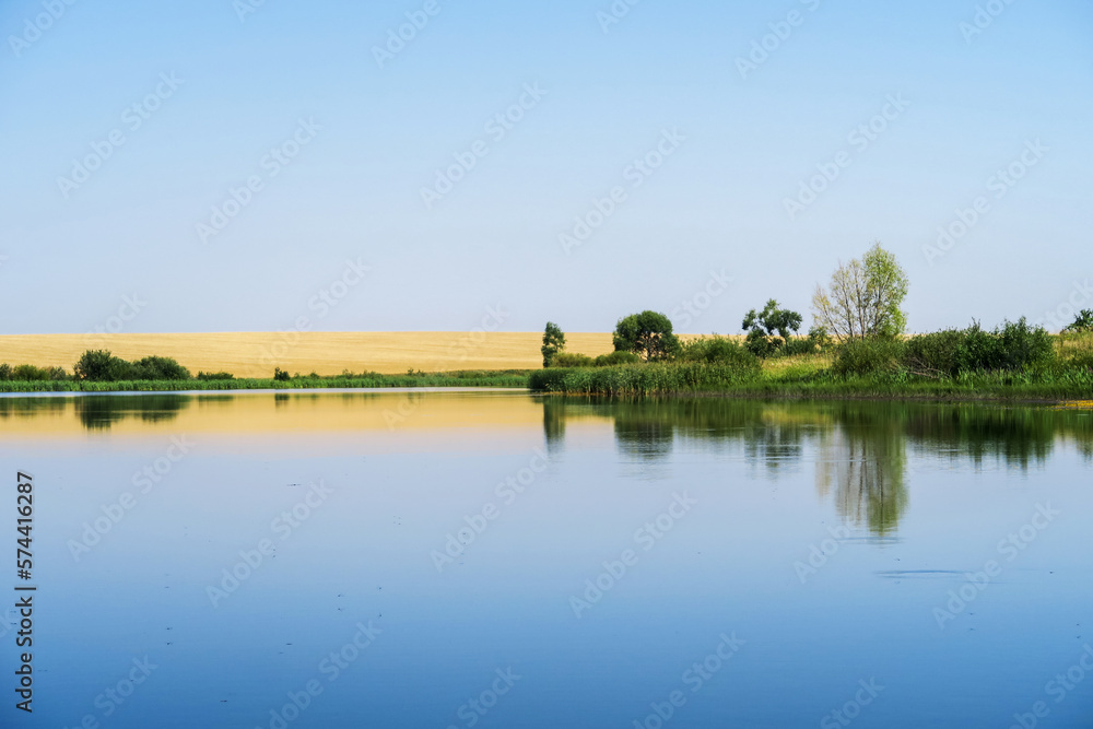 Fototapeta premium Reflection of the sky with clouds on the shore of a large lake on a sunny summer day.