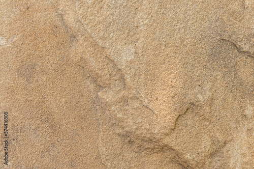 Stone wall is sand-colored with dark spots and bulges. Textured background of stone color sand close-up.