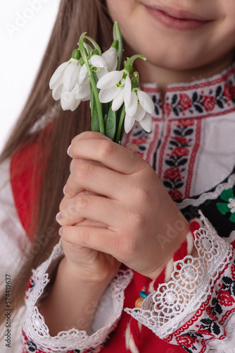 Bulgarian girl in traditional folklore costumes with spring flowers snowdrop and handcraft wool bracelet martenitsa symbol of 1 March Baba Marta national holiday, martisor day