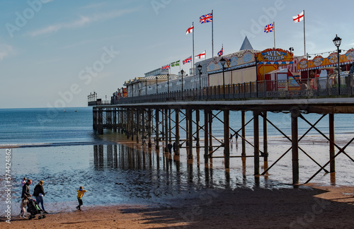 Pier at the English Rivera. A colourful picture of families on holiday and enjoying the winter sunshine at the seaside. Reflective water on a bright day.  © Doodeez