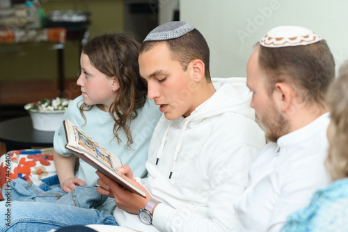 Jewish family celebrate Passover Seder reading the Haggadah. Young jewish man with kippah reads the Passover Haggadah. photo