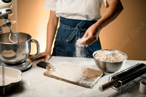 view on hand of woman pouring white flour on wooden cutting board on the table