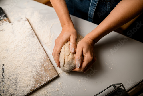 Foto Top view on female chef hands kneading raw bread dough on wooden board