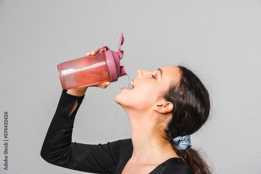 Fitness model exercises with dumbbells and drinks water from a sports bottle Fitness model exercises with dumbbells and drinks water from a sports bottle