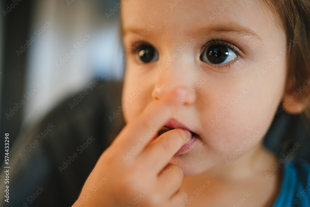 Close-up portrait of a baby girl sitting at table in highchair and eats herself with hands from bowl. Blurred background. Healthy eating for kids. Child's Close-up portrait of a baby girl sitting at table in highchair and eats herself with hands from bowl. Blurred background. Healthy eating for kids. Child's