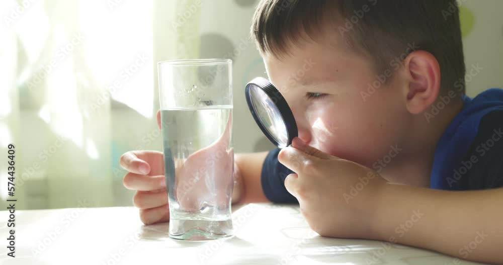 The child boy looking at water in a glass through magnifying glass The child boy looking at water in a glass through magnifying glass