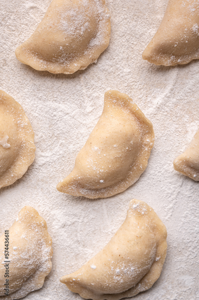 Fresh dumplings in flour on a light background. Pattern, background. Homemade craft production, national traditions, Ukrainian cuisine