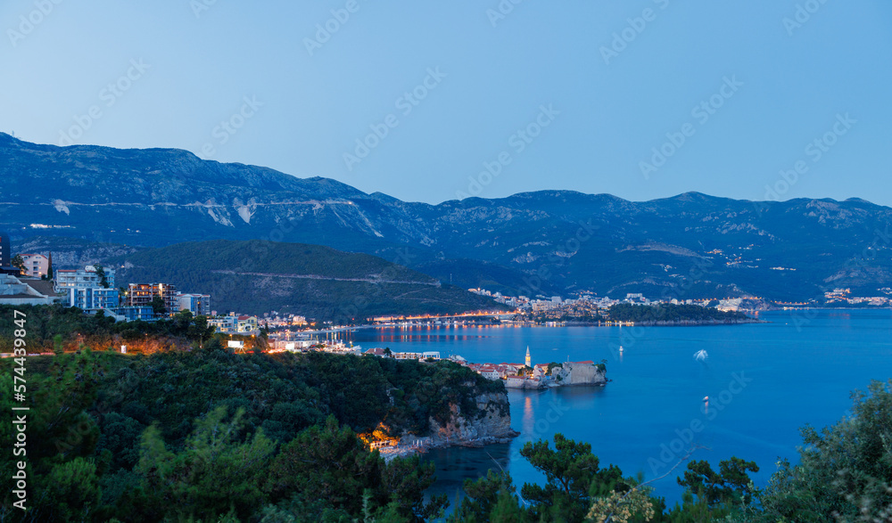 Night city with electric lights against the backdrop of slopes of the Montenegrin mountains and the starry sky near the Adriatic Sea