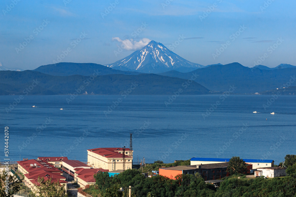 Houses on the shores of the Pacific Ocean, against the backdrop of a volcano, a clear sunny day. Kamchatka.
