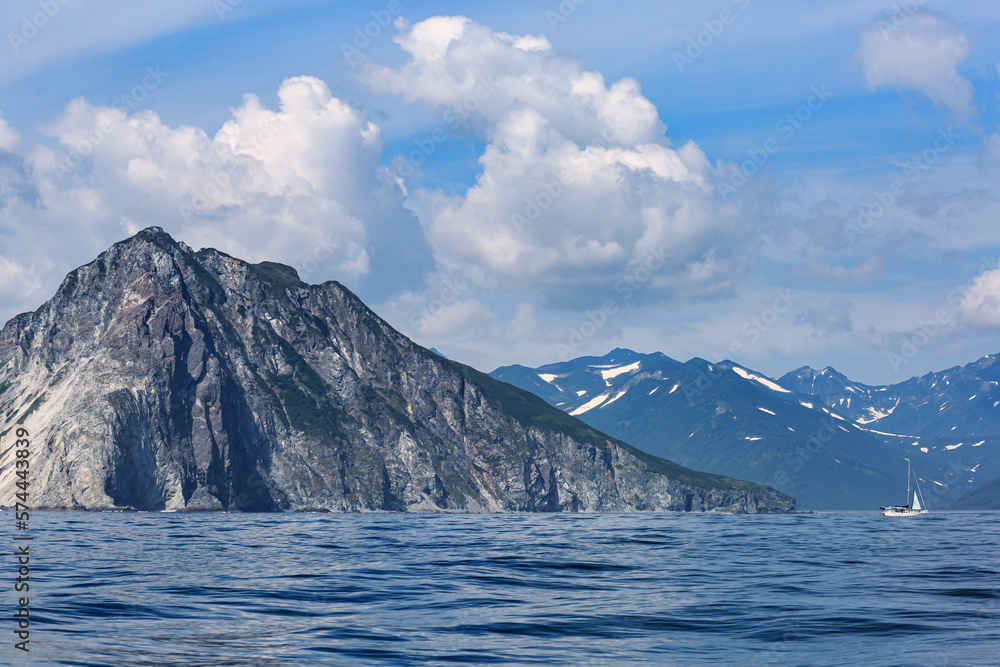 Rocks and mountains of various shapes, in the Pacific Ocean, against the backdrop of a volcano, a clear sunny day, Kamchatka.