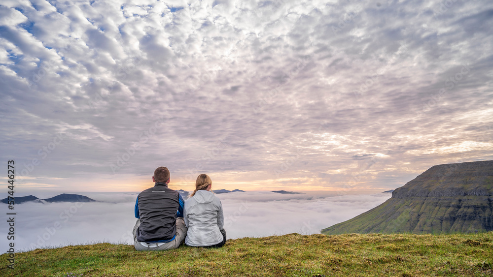 Ein sportliches und aktives Pärchen genießt den Sonnenuntergang über den Wolken auf den Sornfelli auf der Insel Streymoy auf den Färör Inseln. 