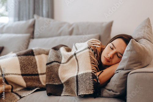Beautiful serene woman sleeping on comfy sofa under warm cozy plaid in modern living room. Healthy daytime nap, tiredness relief, repose and relaxation during day, lazy weekend at home.