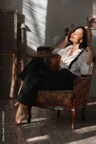 attractive relaxed brunette woman in a chair in the rays of the sun from window.