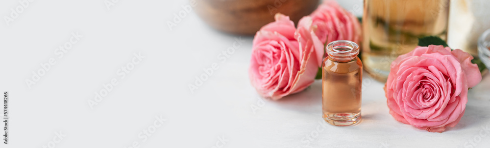 Aromatherapy. Pure organic essential rose oil concept. Elixir with plant based floral herbal ingredients. Pink flowers extract. Spa atmosphere with candle, towel. White background. Banner copy space Aromatherapy. Pure organic essential rose oil concept. Elixir with plant based floral herbal ingredients. Pink flowers extract. Spa atmosphere with candle, towel. White background. Banner copy space