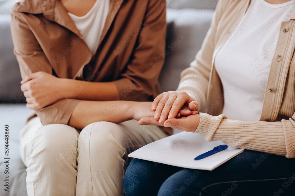 A cute girl at a psychologist's appointment. Psychologist woman holding her patient's hands. Family problems, teenage troubles. Talking with a therapist, advice, help concept.