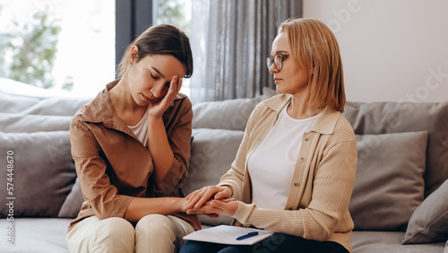 A young girl came for a consultation with a psychologist. She is very ashamed and covers her face with her hands. The psychologist supports her and strokes her head.
