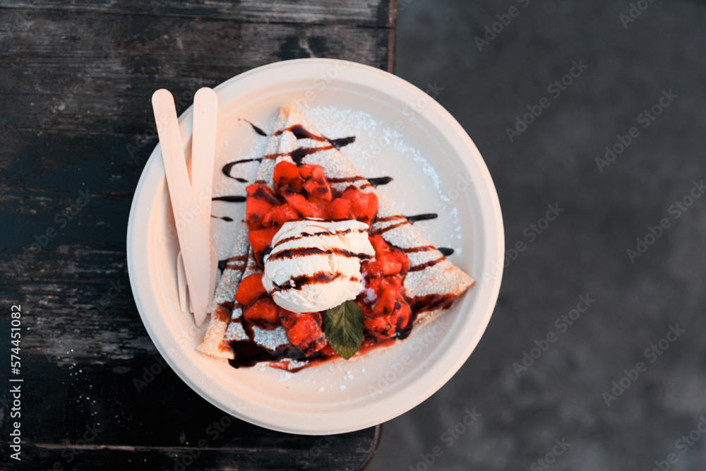 One scoop of vanilla ice cream on top of strawberries on top of crepe with chocolate and powdered sugar
