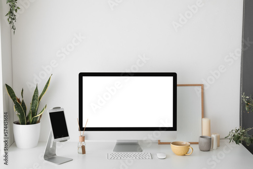 Modern workplace with computer and tablet near light wall