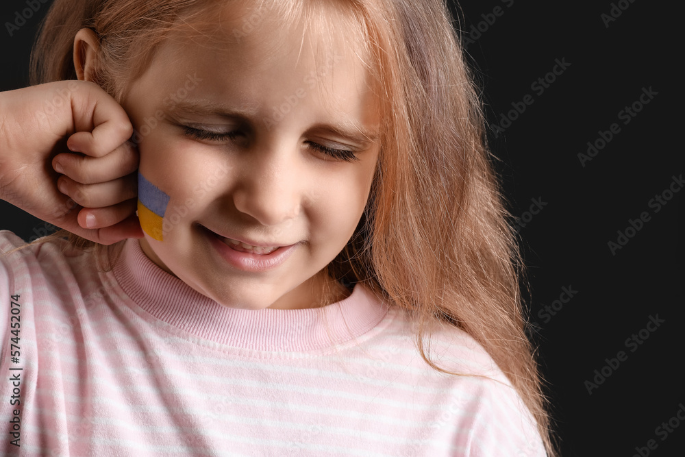 Little girl with drawn flag of Ukraine crying on black background, closeup Little girl with drawn flag of Ukraine crying on black background, closeup