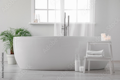 Modern bathtub  houseplant and table with candles in bathroom interior