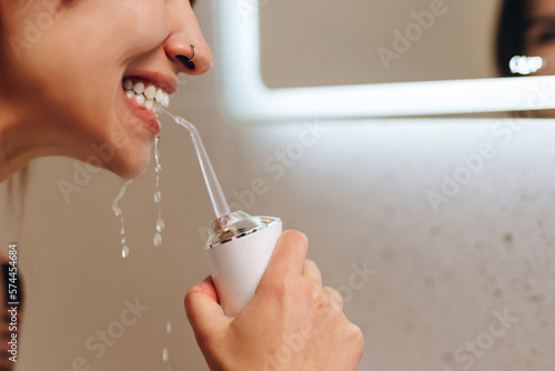 Woman with perfect white smile using portable water flosser or oral irrigator.