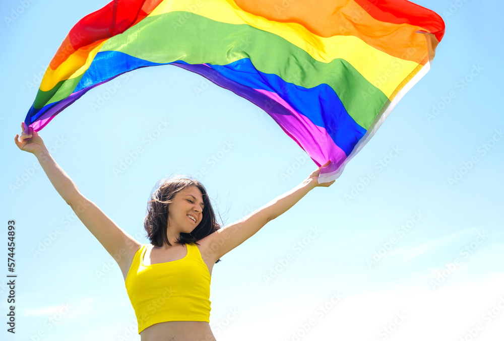 The pride of being special, not like everyone else. A happy woman holds a rainbow flag fluttering in the wind