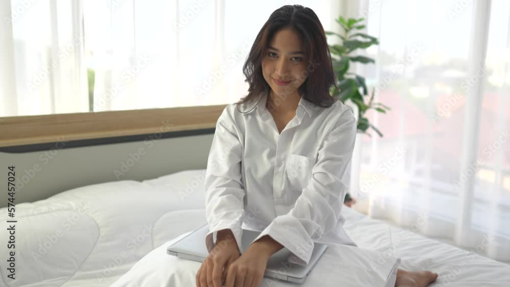 young asian woman using smartphone and laptop when sitting on a bed ...