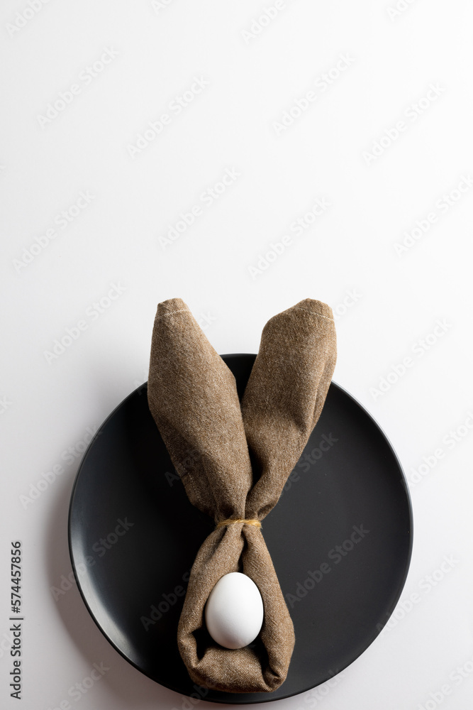 Obraz premium Image of white easter egg and bunny ears on black plate and copy space on white background