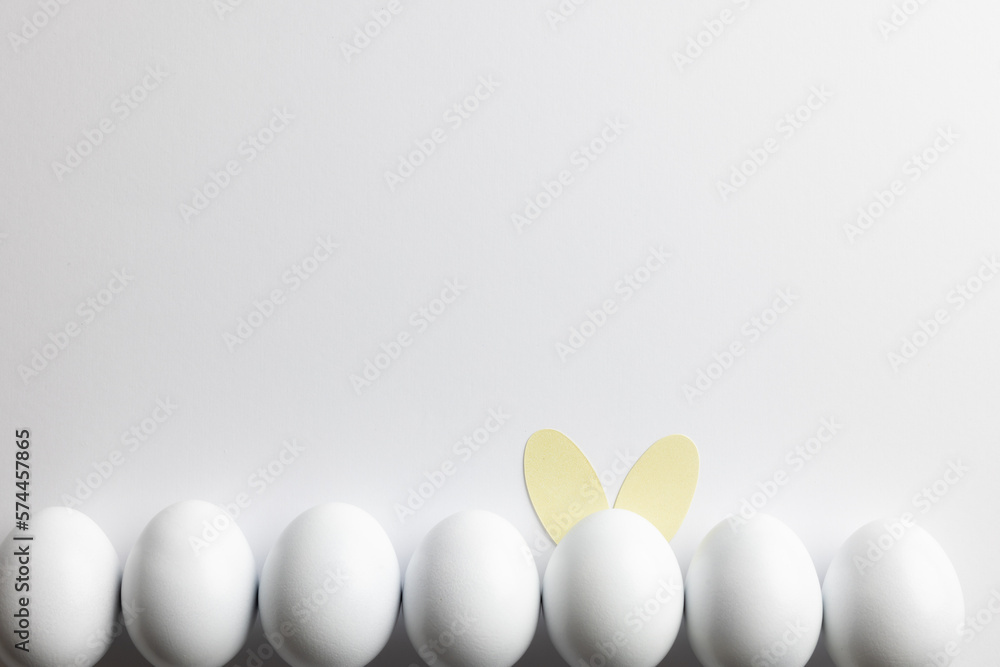 Fototapeta premium Image of row of white easter eggs with bunny ears and copy space on white background
