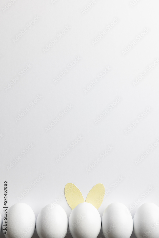 Fototapeta premium Image of row of white easter eggs with bunny ears and copy space on white background