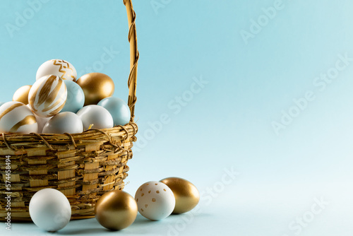 Image of multi coloured easter eggs in basket and copy space on blue background