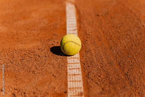 Light orange empty outdoor clay court surface dry grungy ground baseline detail for playing tennis with net in sunny day with yellow green ball, gravel texture background, copy space for text 
