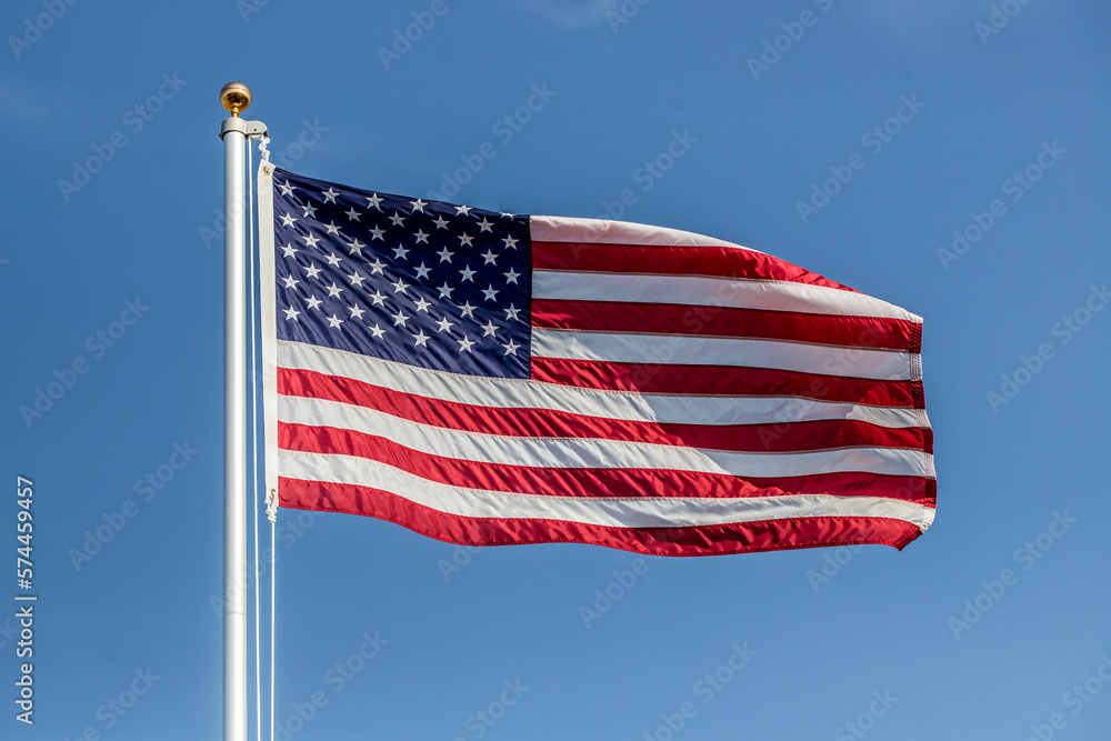 US flag displayed on flagpole with clouds background on a breezy day US flag displayed on flagpole with clouds background on a breezy day
