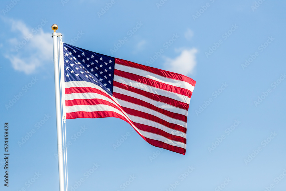 US flag displayed on flagpole with clouds background on a breezy day