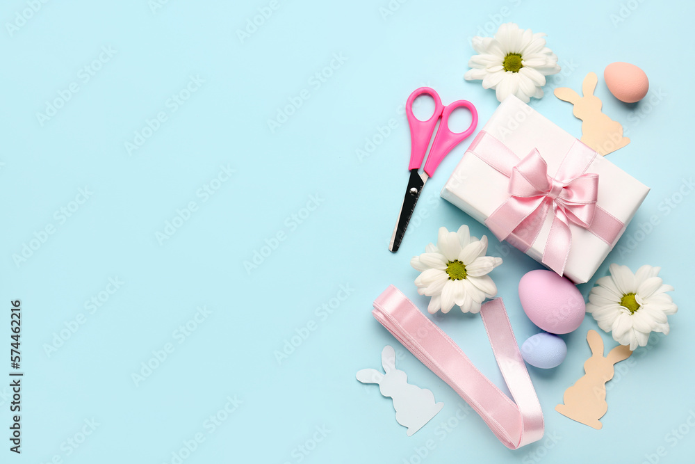 Gift with scissors, Easter eggs, paper rabbits and flowers on blue background