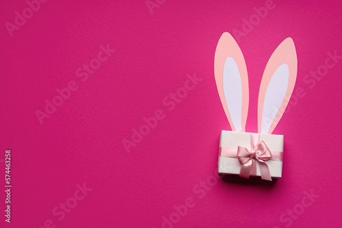 Paper bunny ears and gift box on pink background