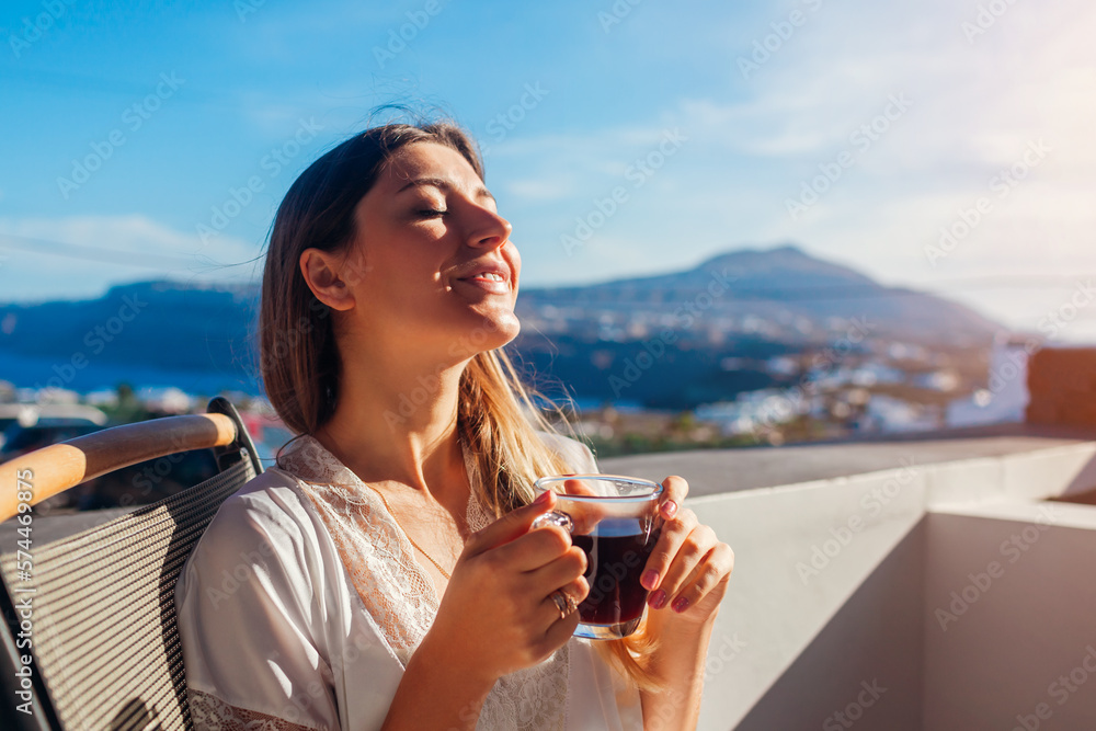 Woman relaxing on hotel terrace drinking morning coffee enjoying Santorini mountain landscape. Breakfast with view - obrazy, fototapety, plakaty 