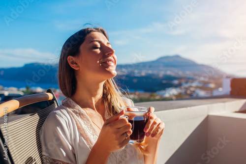 Foto Woman relaxing on hotel terrace drinking morning coffee enjoying Santorini mountain landscape