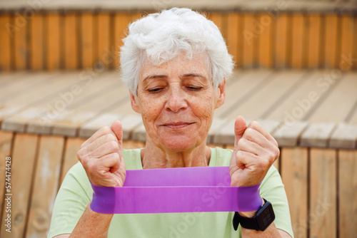 Portriat of old woman with grey short hair training with fitness band outdoow, summer day. photo