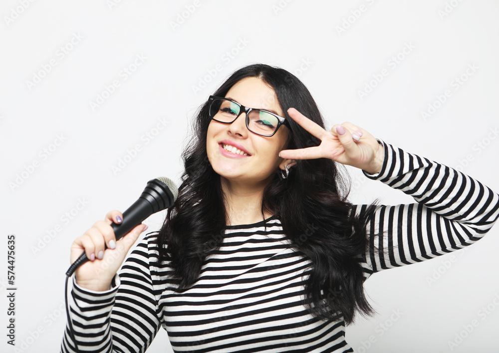 Young curvy woman singer with a microphone over light grey background Young curvy woman singer with a microphone over light grey background