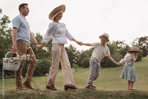 Children, dad and mom play in meadow in sunshine. mother, father and little daughter with brouther walking in field in the sun. Happy young family. concept of a happy family. photo